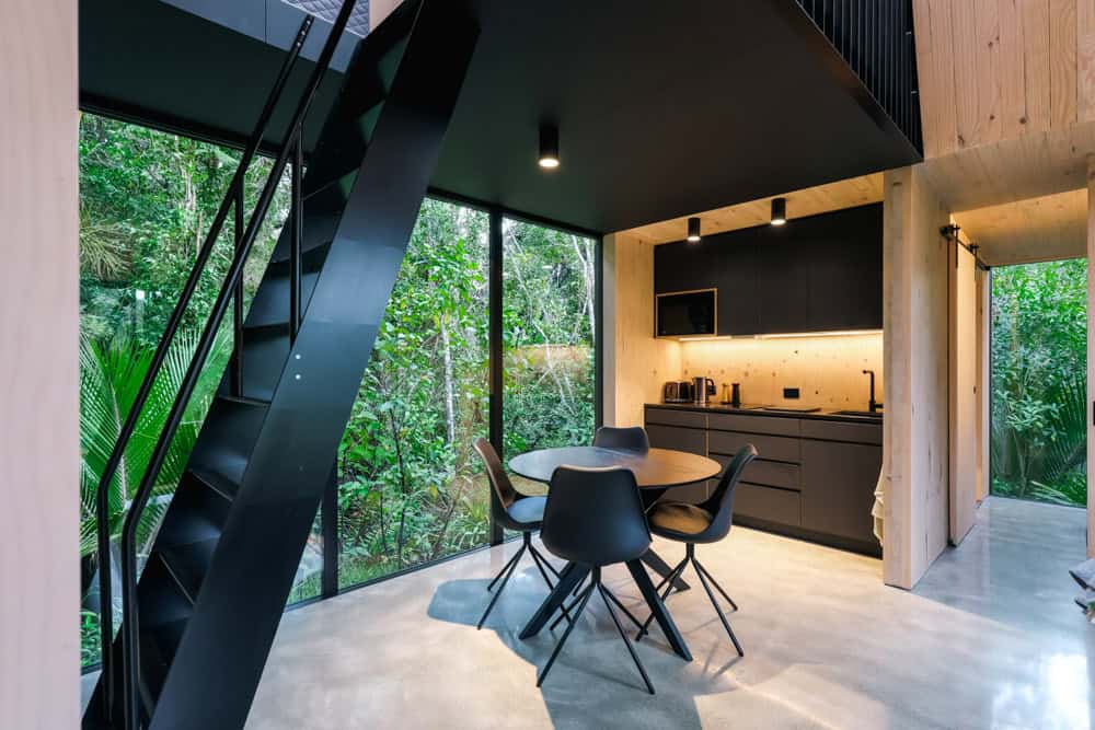 Black kitchen, round dining table, and black stair with forest in the glass