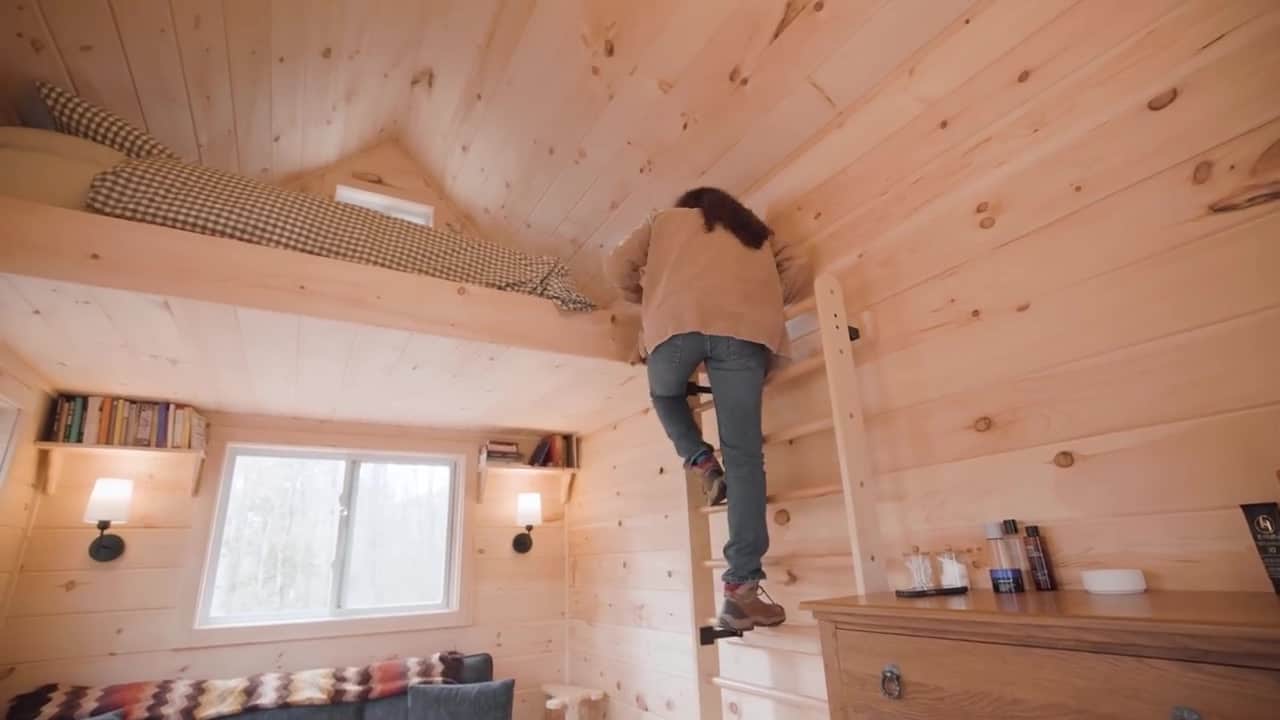 Bree climbing wall-mounted wooden bars into the sleeping loft above the living area of her 144 square foot Maine cabin