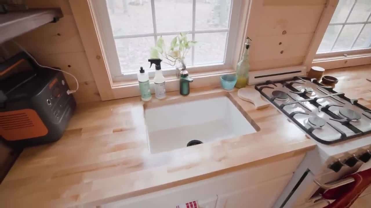 Butcher block counter with a custom undermount sink, a Jackery portable power station on the left, and a white propane cooktop on the right