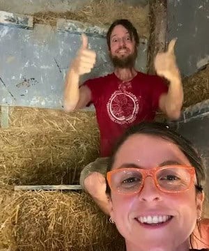 Straw bales stacked in a wall opening, a smiling couple in the frame during construction
