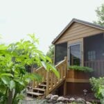 Brian’s tan cabin-style tiny house with screened porch and steps at Tiny Timbers Agrihood in Wisconsin