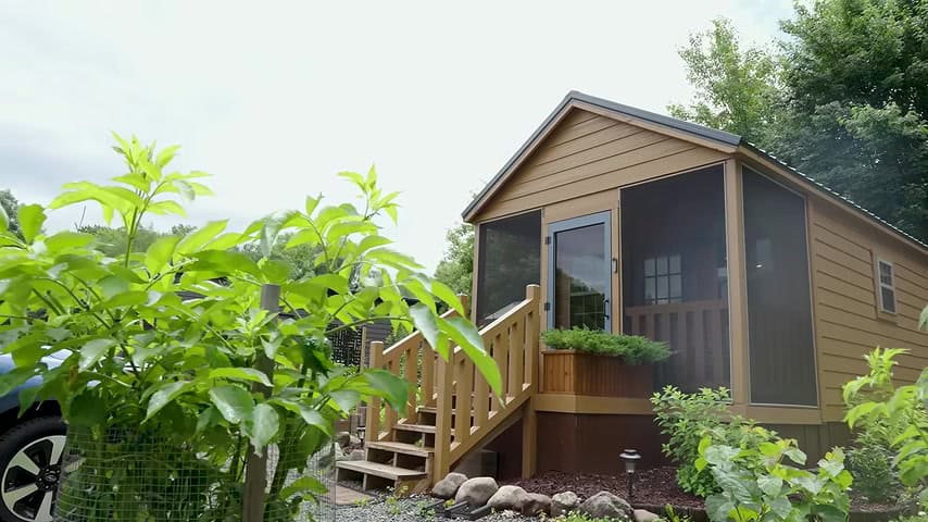Brian’s tan cabin-style tiny house with screened porch and steps at Tiny Timbers Agrihood in Wisconsin