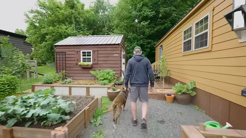Brian walking his dog Stella past raised garden beds and a shed at Tiny Timbers Agrihood