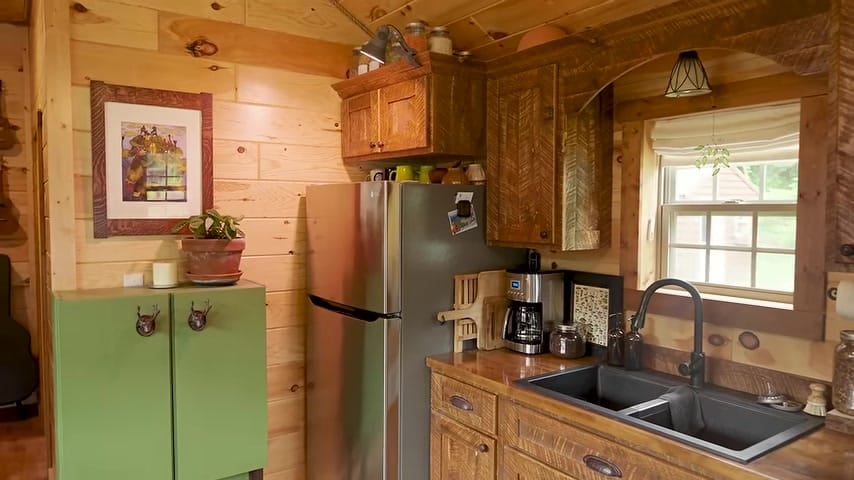 Full-size kitchen with herringbone wood cabinets, black sink, and stainless fridge in Brian’s tiny house