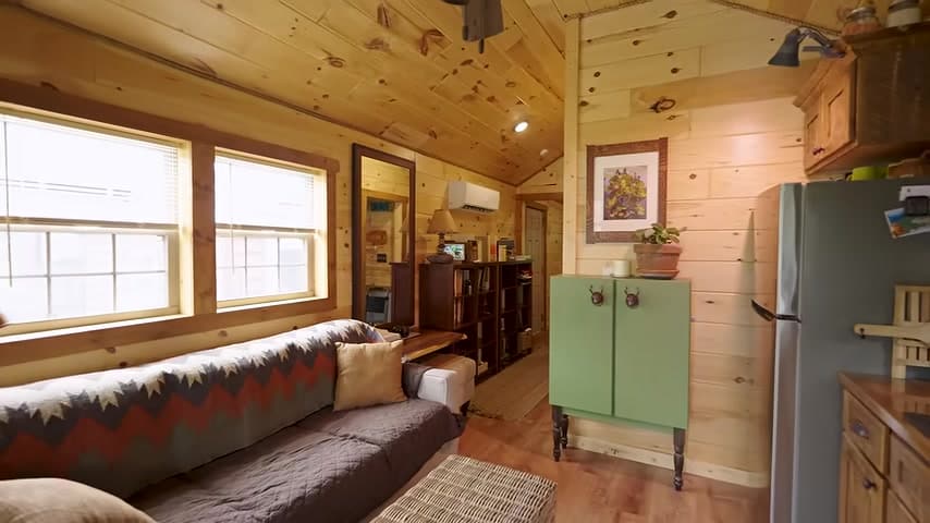 Open living room and kitchen of Brian’s wood-paneled tiny house with sofa and sage cabinet