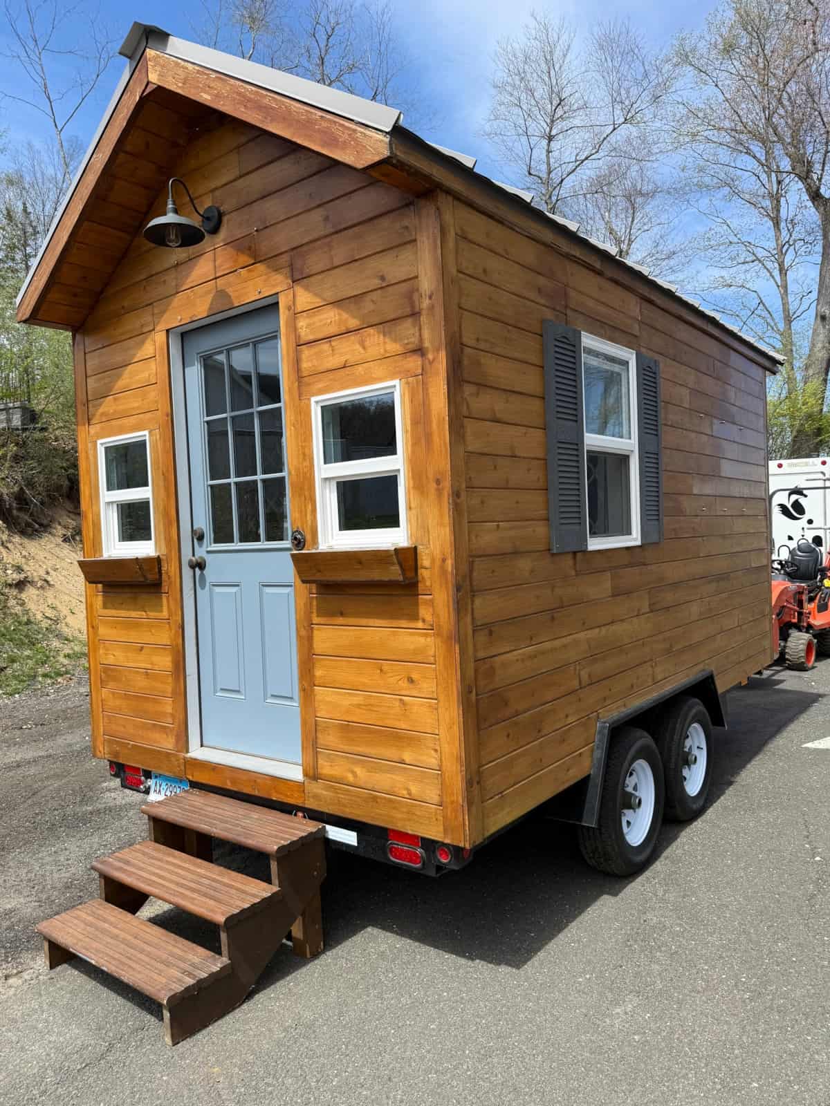 Cedar 7x14 cottage on a dual-axle trailer with a blue door, flower boxes, porch light, and wooden steps in Brookfield, Connecticut