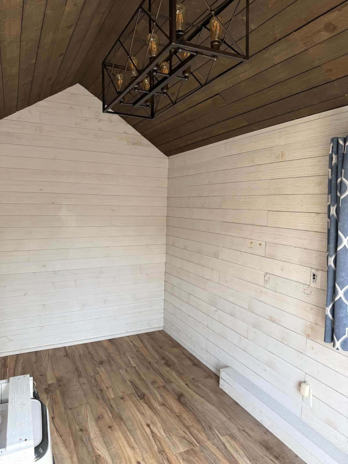 Vaulted dark-wood ceiling, eight-bulb chandelier, white shiplap walls, and empty vinyl plank floor