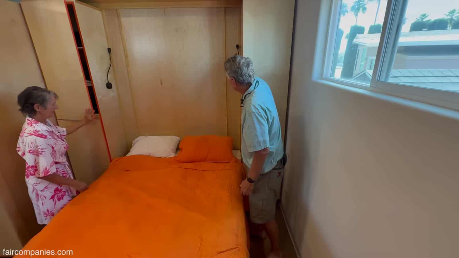 Murphy bed lowered into a queen bed with an orange bedspread