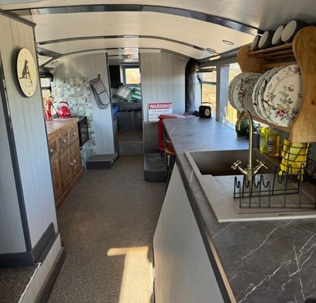Long galley kitchen inside the lower deck of a bus with a sink, plate rack, and wood counters