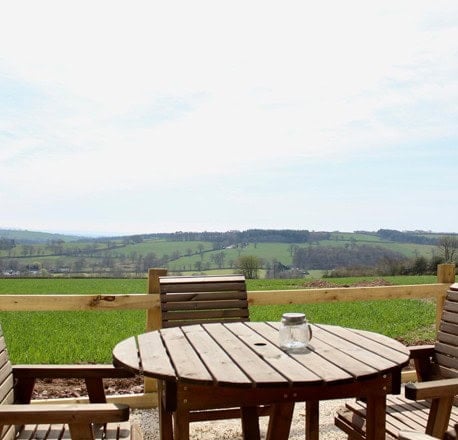 Round wooden patio table and chairs looking out over green fields and hills