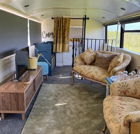 Upstairs sitting room with floral armchairs, a sofa, a TV stand, and a bed visible at the front