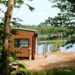 Wood-sided Cove Cabin on a rocky lakefront clearing, glass-rail deck, canoe paddle by the door, summer trees and still water