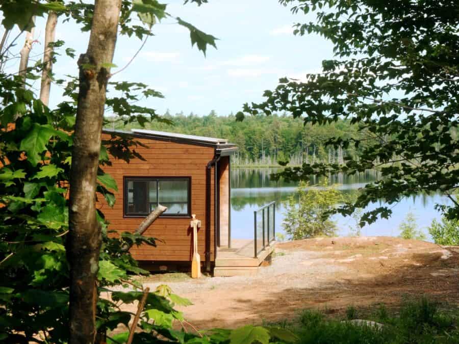 Wood-sided Cove Cabin on a rocky lakefront clearing, glass-rail deck, canoe paddle by the door, summer trees and still water