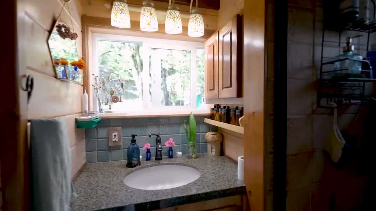 Bathroom vanity with a speckled granite counter, oval sink, teal tile backsplash, and a window looking into the trees