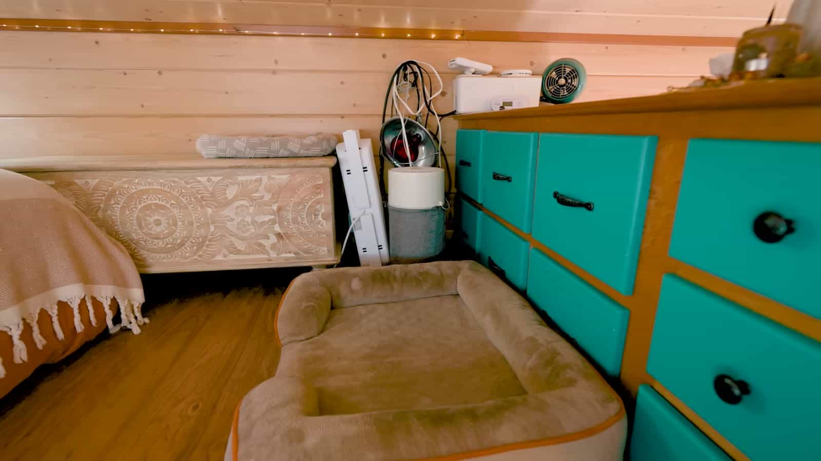Teal-painted built-in dresser drawers beside a dog bed and a carved chest in the loft