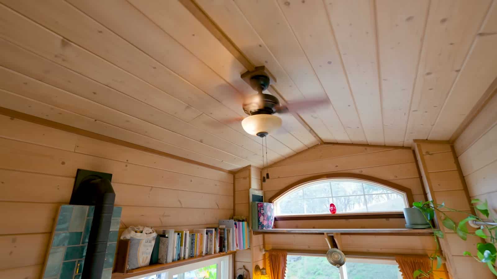 Pine loft ceiling with a ceiling fan, an arched window, and a long bookshelf along the wall