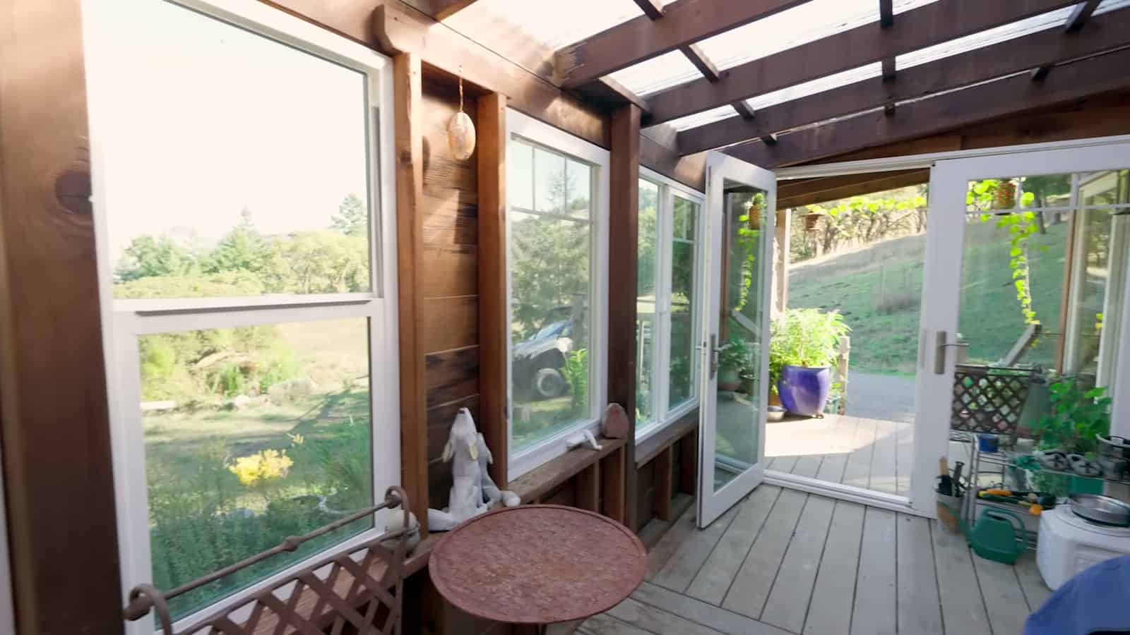 Covered porch with a wall of windows and open French doors looking out to the garden and hills