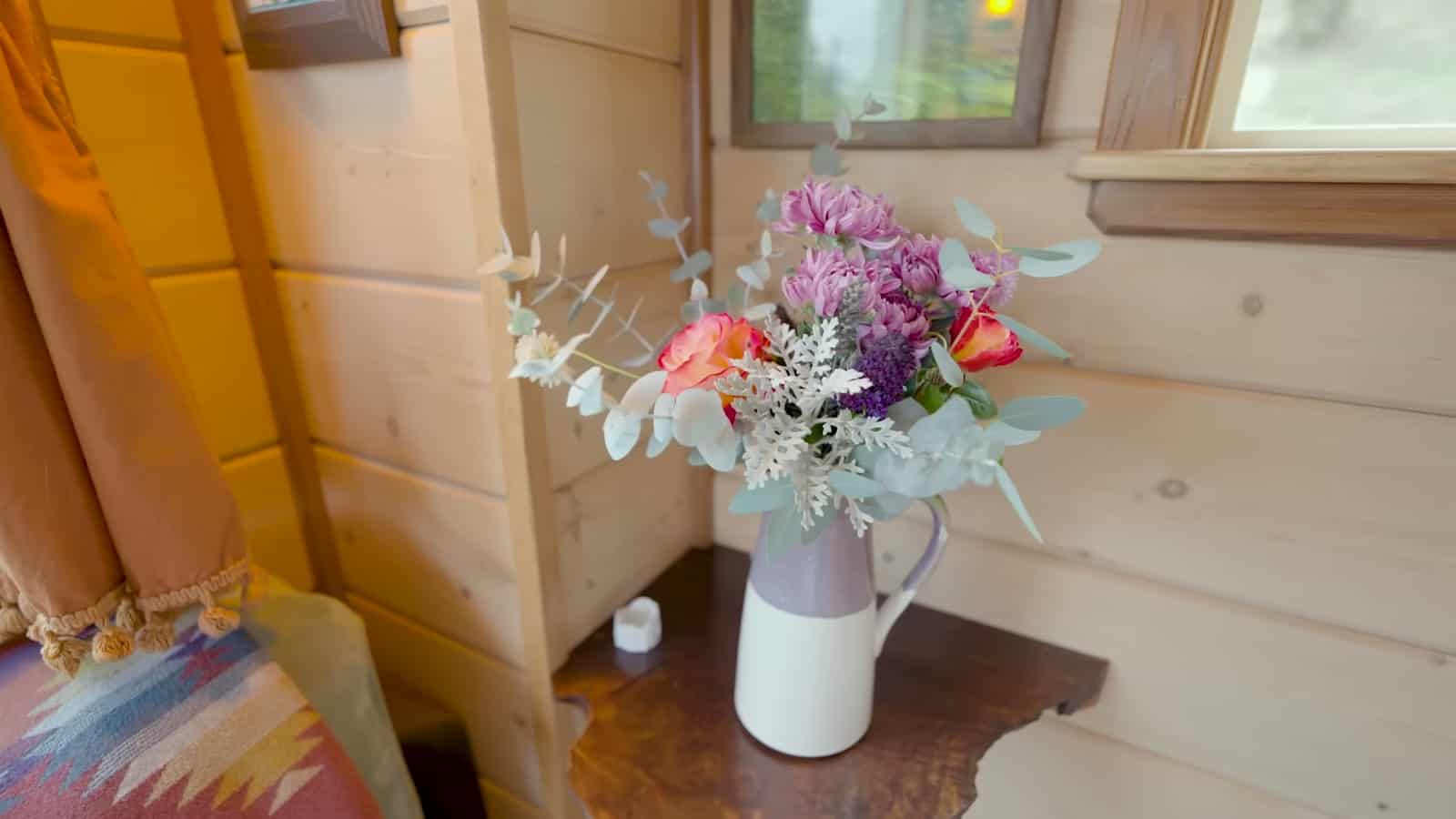 Live-edge wood side table holding a pitcher of fresh flowers beside a blue recliner
