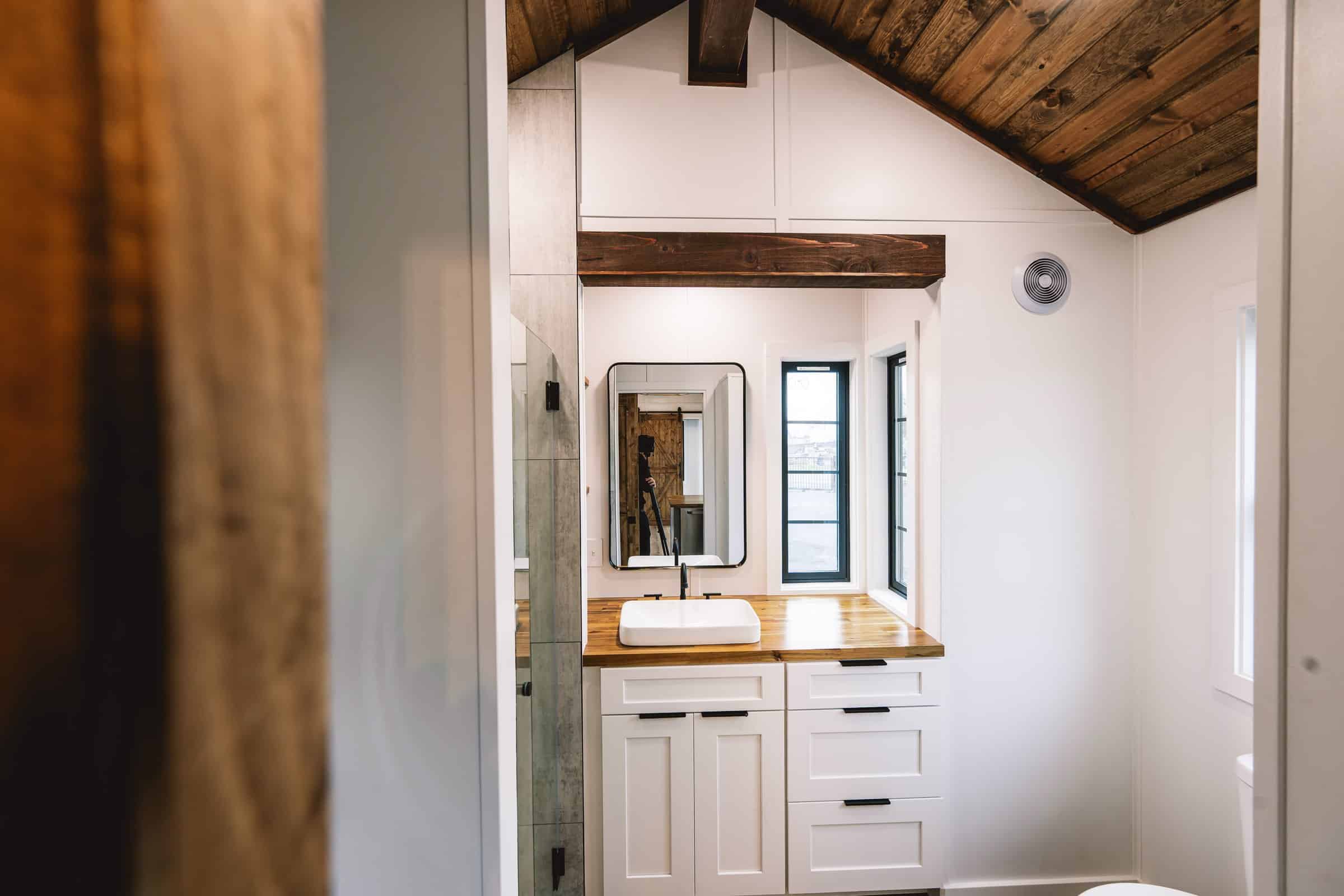 Callisto bathroom with butcher-block vanity, white vessel sink, black-framed mirror, painted shiplap, stained T&G ceiling, and a glimpse of a standard residential toilet