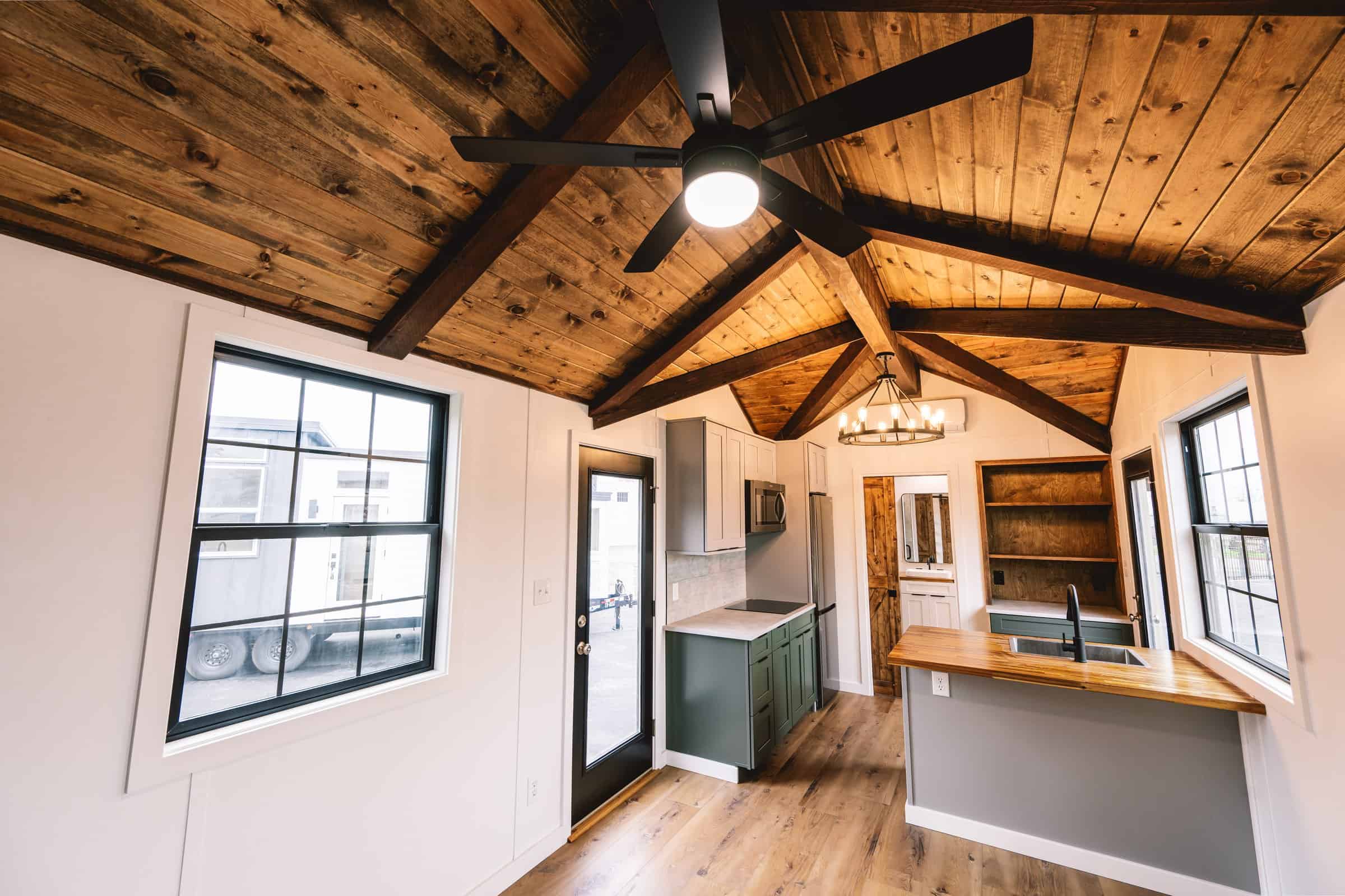 Callisto interior looking toward the kitchen: stained wood T&G ceiling with open beams, painted shiplap, LVP, black-grid windows, butcher-block island, 2-burner induction, apartment-sized fridge