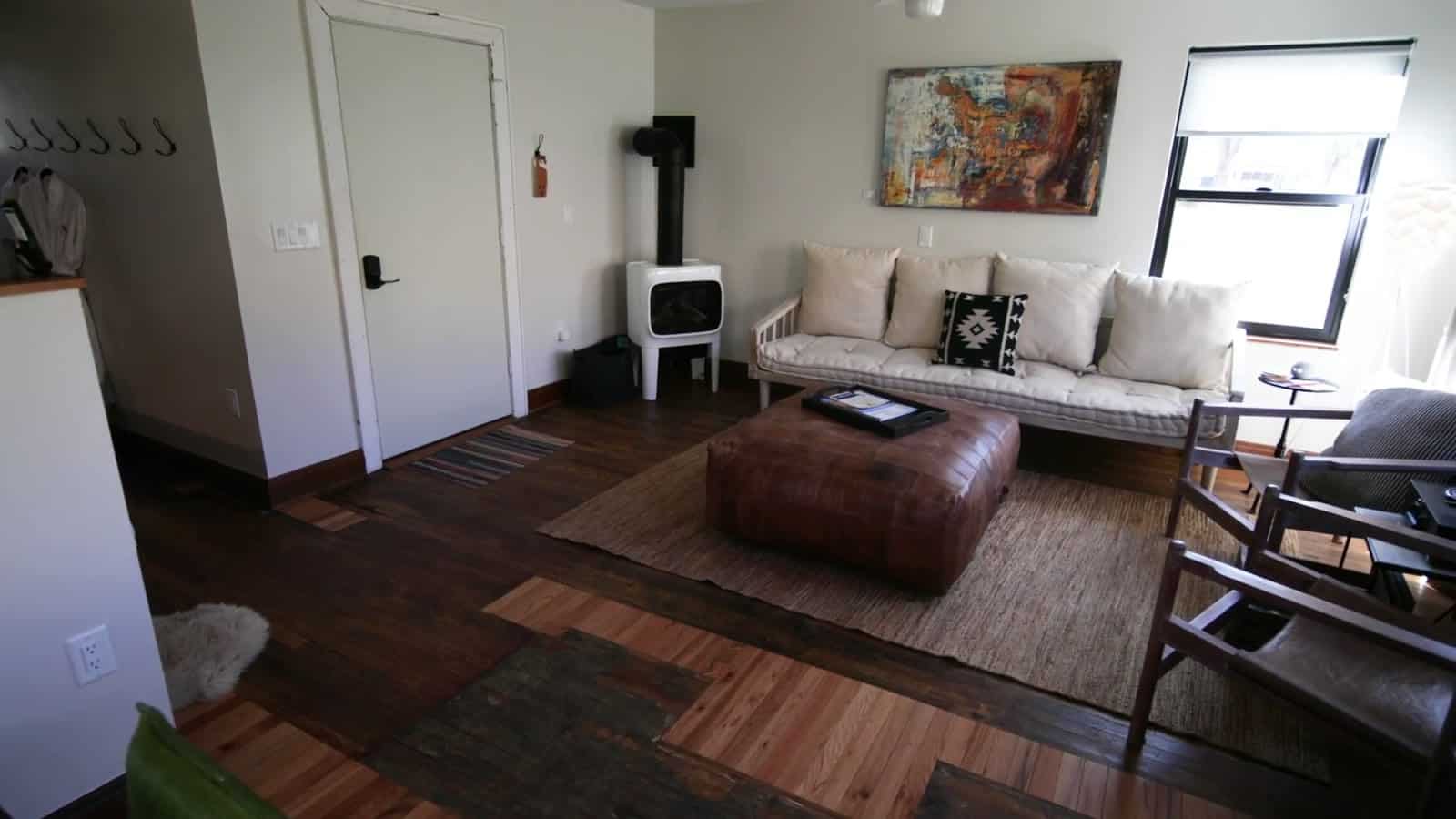 Bright open-concept living room in a Camp V cabin with sofa, ottoman, and wood stove