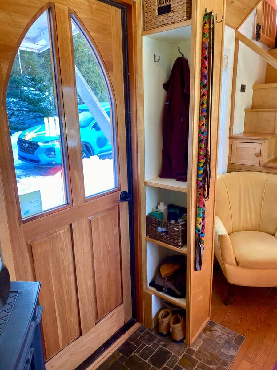 Arched wooden front door with built-in coat cubby and shoe storage inside the tiny house