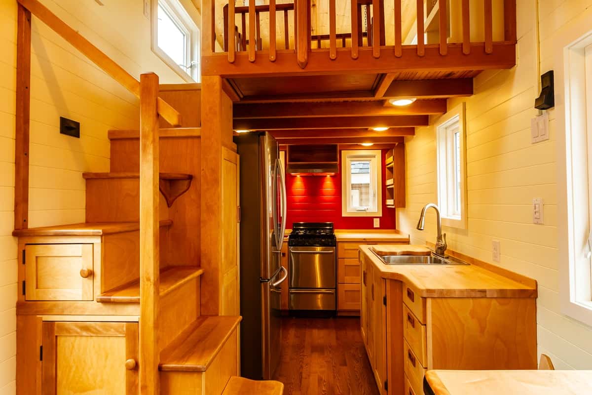Galley kitchen past the storage stairs with butcher block counters and stainless fridge