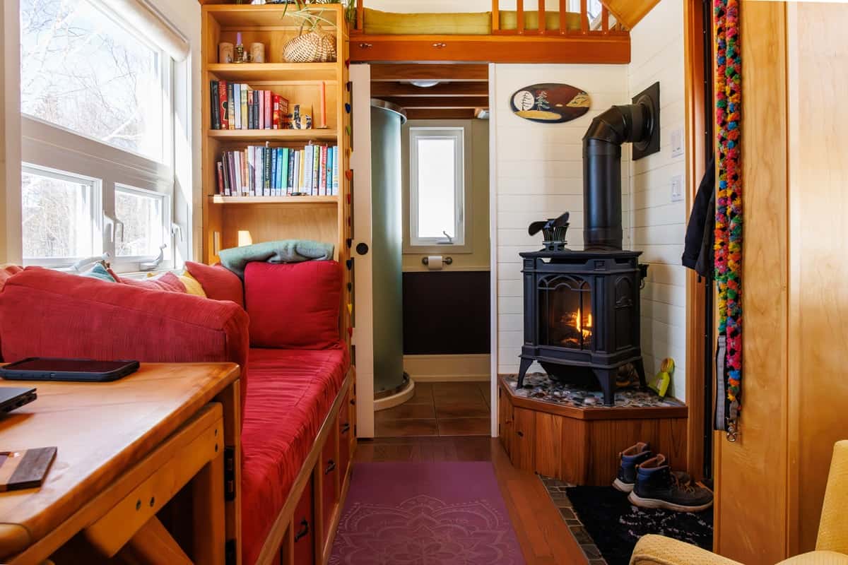 Tiny house living room with red built-in couch, bookshelves and black Napoleon propane stove