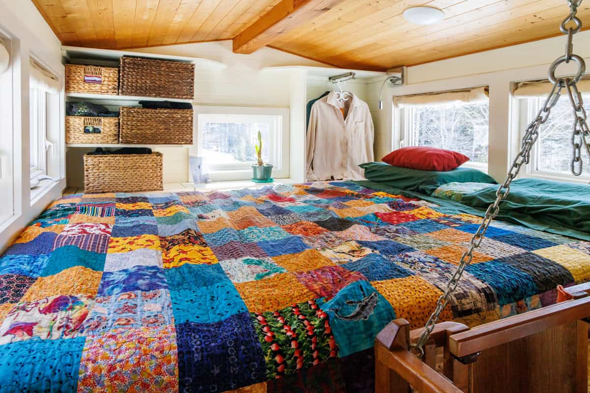 Main loft bedroom with colorful patchwork quilt, storage baskets and windows