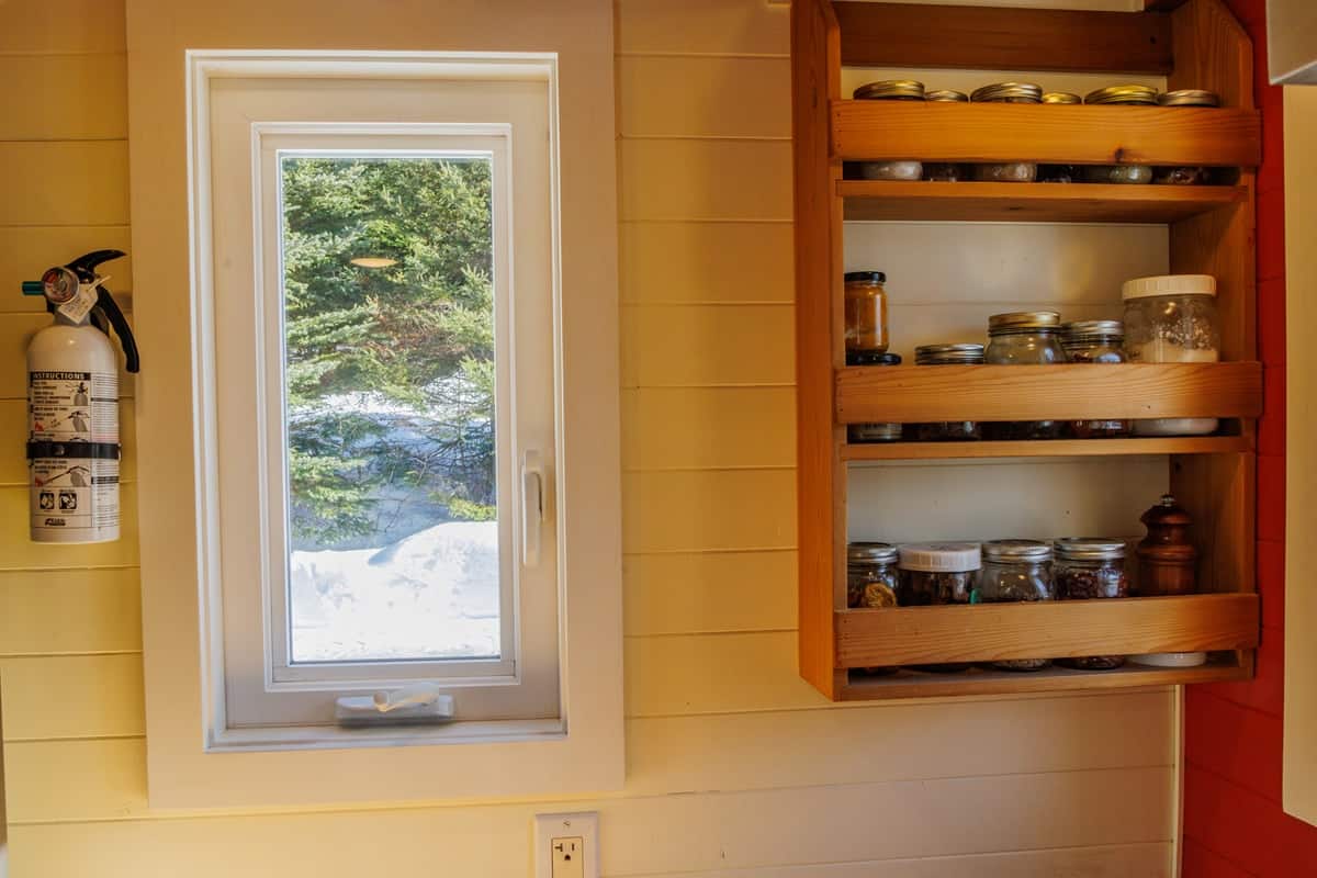 Recessed wooden spice rack built into the wall beside a window