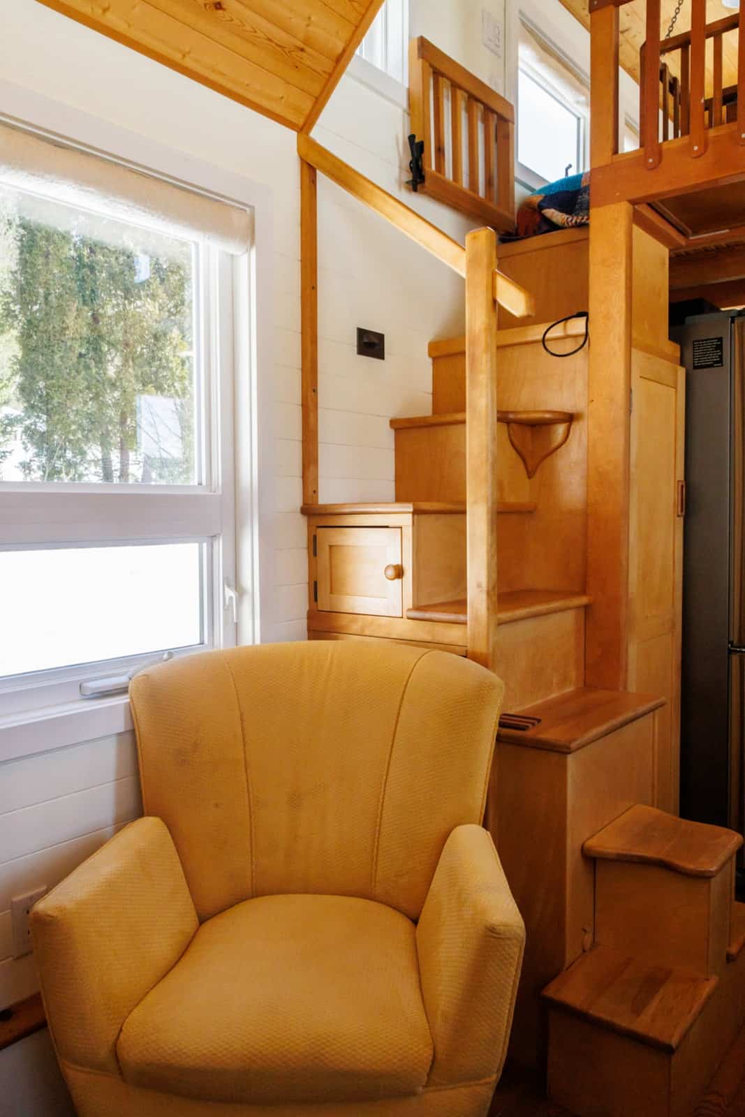 Wooden storage staircase beside a yellow armchair in the tiny house