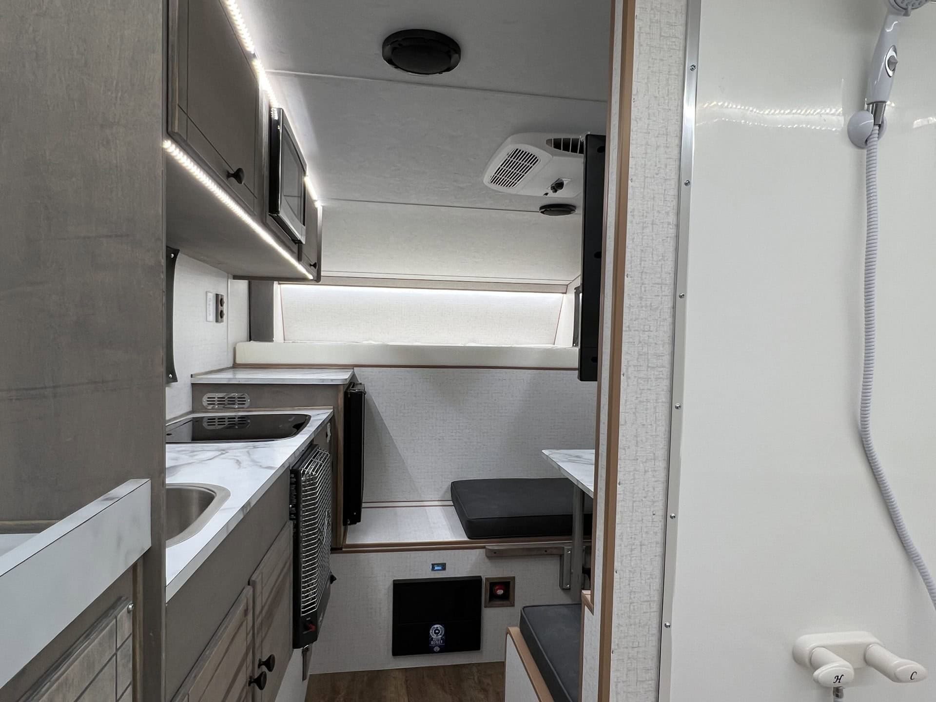 View into the Capri Retreat from the back door, past a handheld shower wand, to the galley, dinette, and cab-over bed