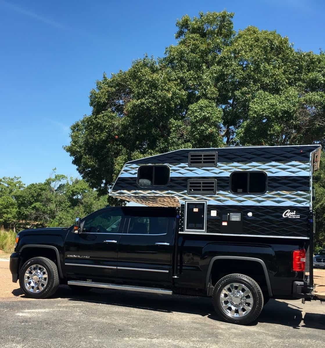 Capri Retreat cab-over truck camper with silver and black striping on a black pickup under oak trees