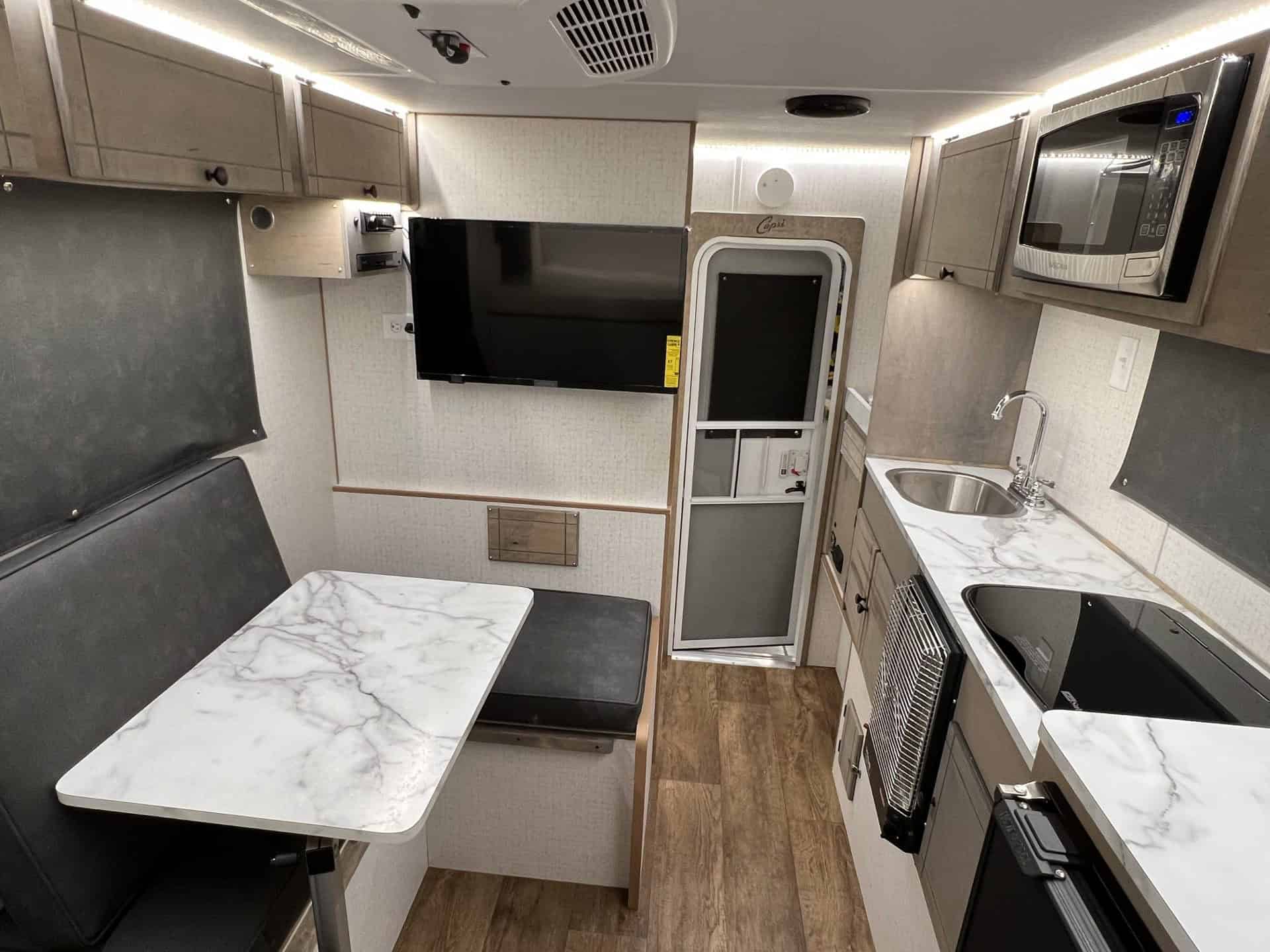 Capri Retreat interior with a marble-look Lagun table dinette, galley sink, microwave, TV, and back door with screen