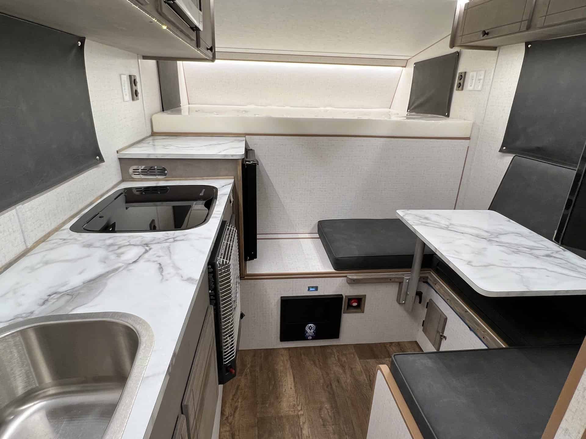 Capri Retreat living space: 60x80 cab-over sleeper, galley counter, dinette benches, wood-grain floor