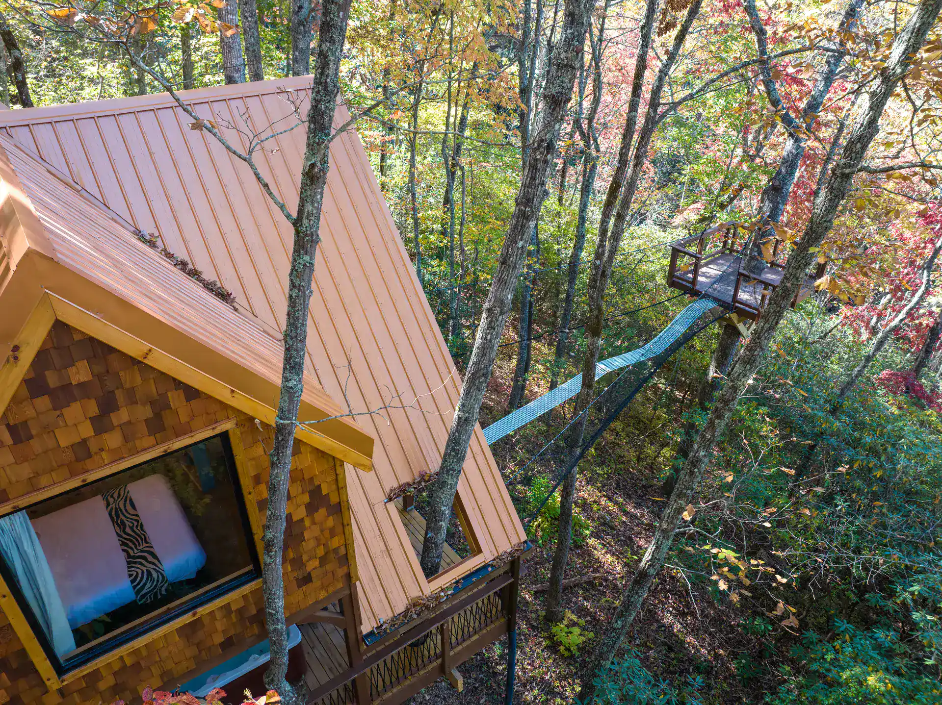 Aerial exterior of The Carpentree: copper roof, decks, sky net, and hot tub below among the trees
