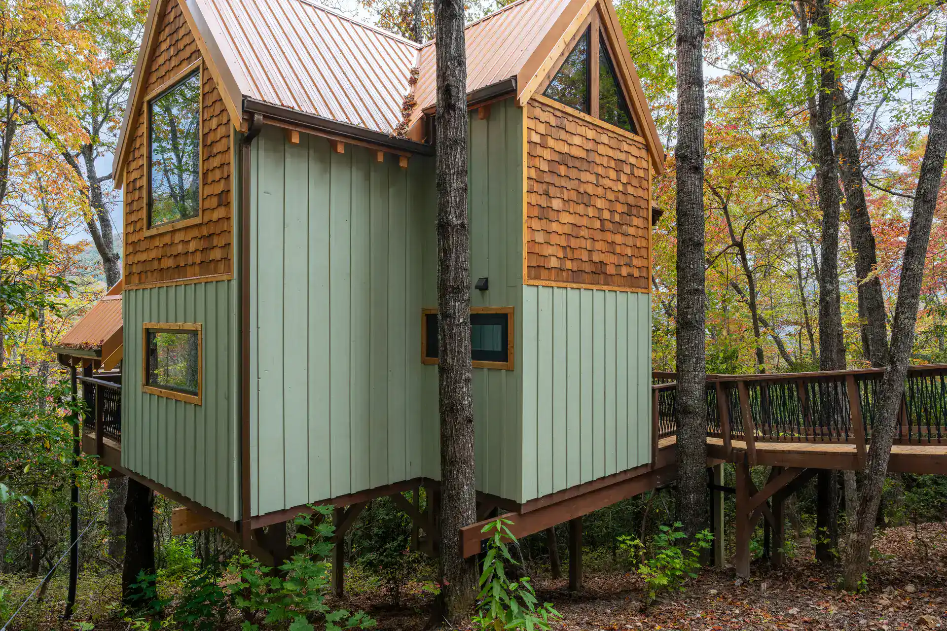 Ground-level exterior of The Carpentree with sage board-and-batten and the treehouse structure above