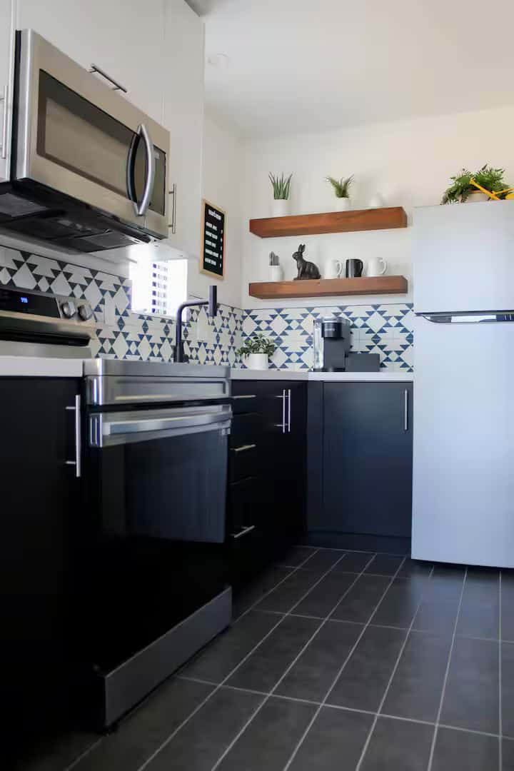 Full-size kitchen with black cabinets, patterned tile backsplash, open wood shelves and a white refrigerator