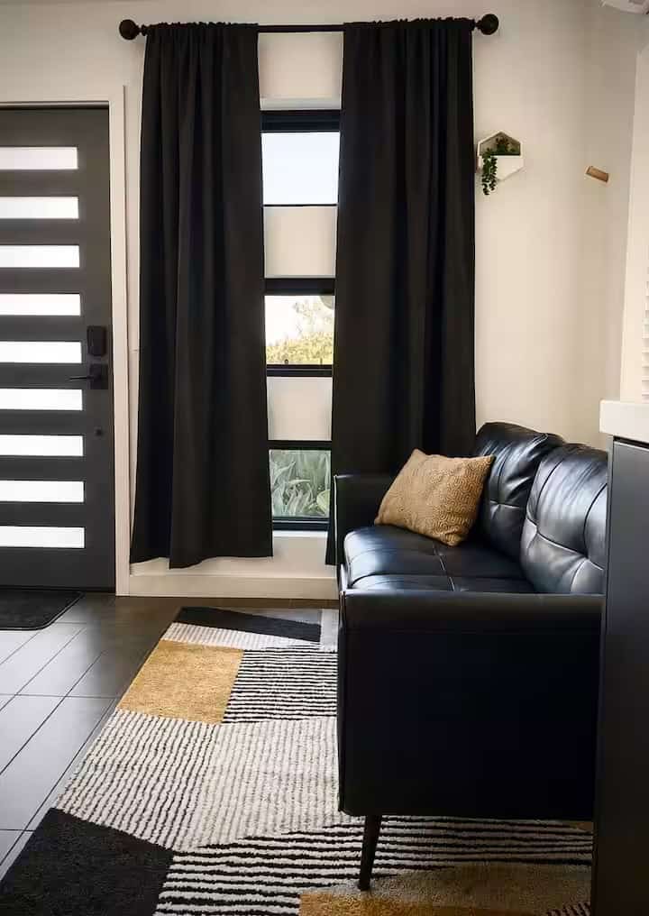 Downstairs living room with a black leather sofa, patterned rug and tall windows