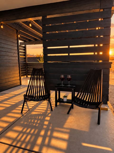 Covered patio with slatted privacy walls and two lounge chairs at sunset