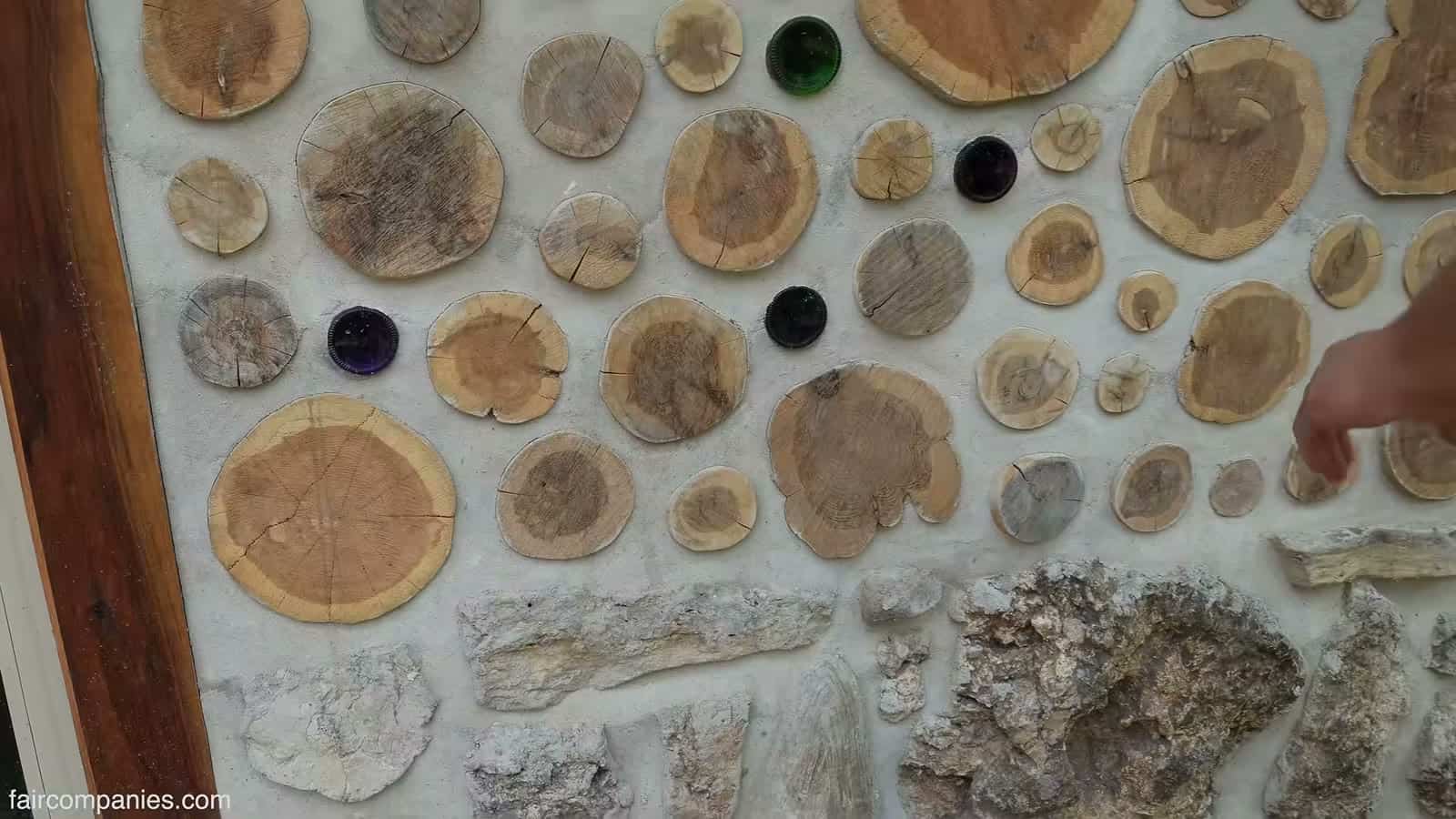 Close-up of a cordwood wall with cedar rounds of many sizes set in pale mortar, with a few dark green and purple bottle bottoms, beside a wood door frame