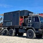 Custom mobile fortress built on a military truck with outdoor gear and bikes.