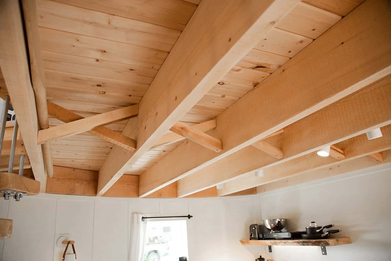 Light wood loft joists over a white-paneled kitchenette wall, a live-edge shelf, and the start of a wood-tread stair