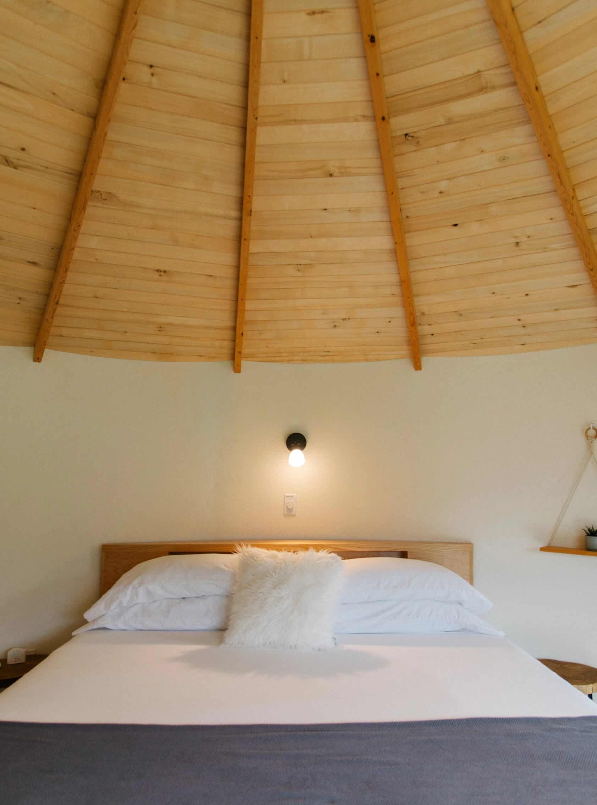 King bed against a curved cream wall under a conical wood-plank silo ceiling