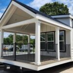 2026 Clayton Wheeler on the Springville lot: white board-and-batten, black porch rail, hitch marked 169, dark roof, gravel lot