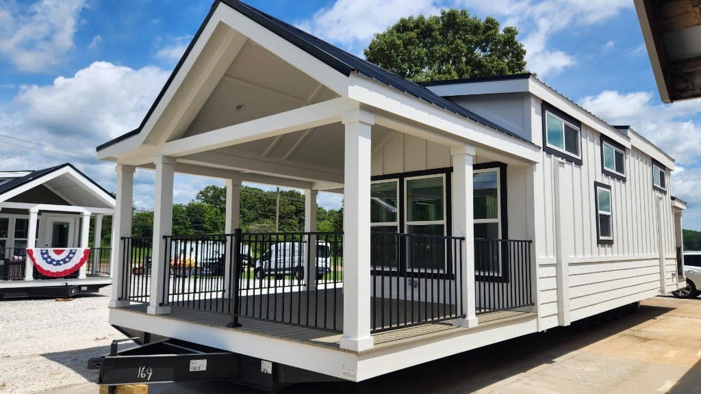 2026 Clayton Wheeler on the Springville lot: white board-and-batten, black porch rail, hitch marked 169, dark roof, gravel lot