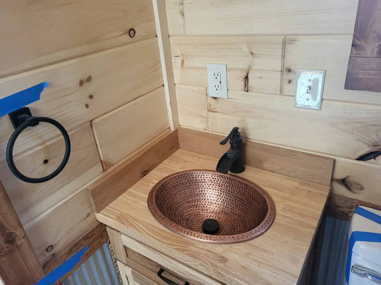 Hammered copper vessel sink with an oil-rubbed bronze faucet on a wood vanity against pine walls in the Cherokee cottage bathroom