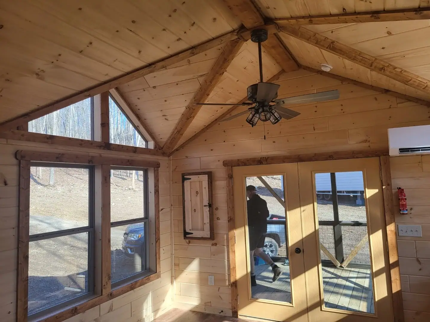 Vaulted knotty-pine living room in the Cherokee cottage with gable-end clerestory windows, a ceiling fan, and French doors to the porch