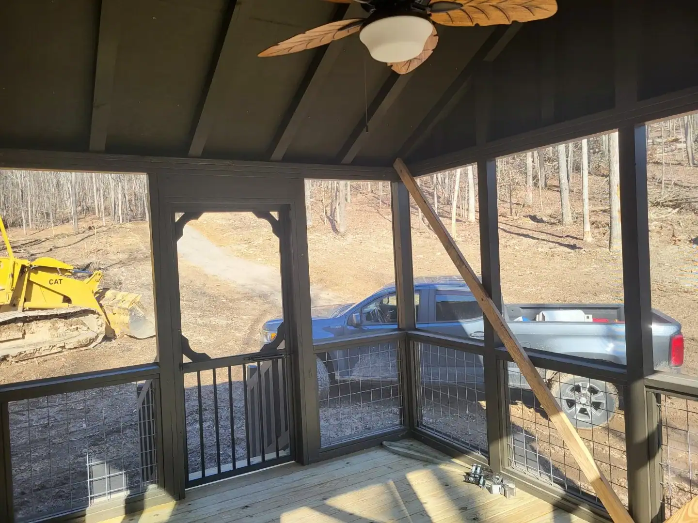 Inside the Cherokee cottage's screened porch, with a leaf-blade ceiling fan, painted wood ceiling, and screened walls looking out to the woods