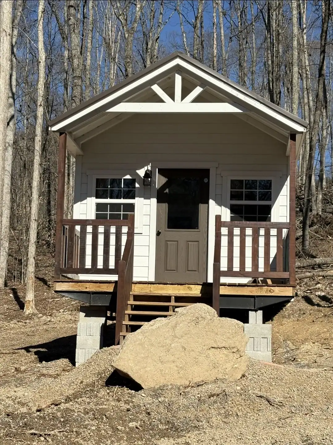 Front of the Woodland cottage with white lap siding, decorative gable trim, a brown railed front porch, and wooden steps on concrete-block piers